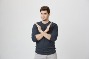 Serious confident angry european man with stubble in casual clothes, keeping hands in stop gesture, crossing arms, frowning his face, as if saying: Stop that. Body language.